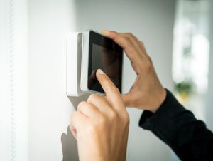 A person adjusts a wall-mounted smart thermostat by touching the screen, controlling indoor temperature settings in a modern home environment.